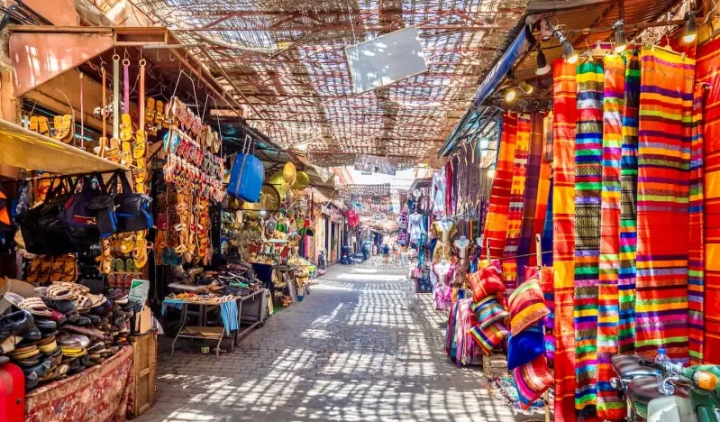A narrow alley filled with vibrant cloths and bags, showcasing local Moroccan textiles and crafts.
