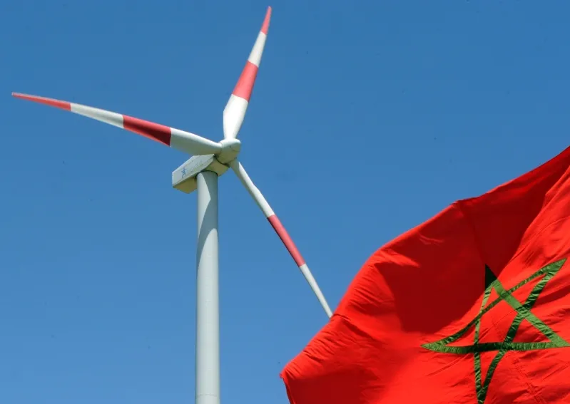 A red flag with a white star stands beside a wind turbine, symbolizing Morocco's energy landscape and national identity.