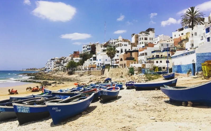 Fishing boats lined up on a sandy beach in Morocco, showcasing a vibrant Morocco holidays atmosphere.