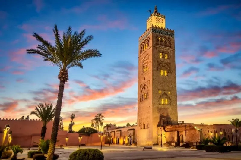 Sunset view of the Marrakech mosque clock tower, highlighting its silhouette against a colorful sky.