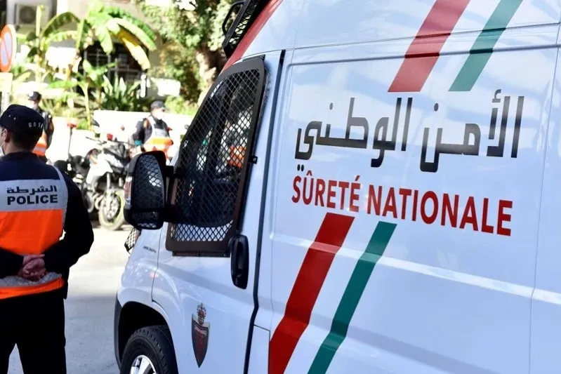 A man wearing an orange vest stands next to a white van, showcasing travel safety in Morocco.