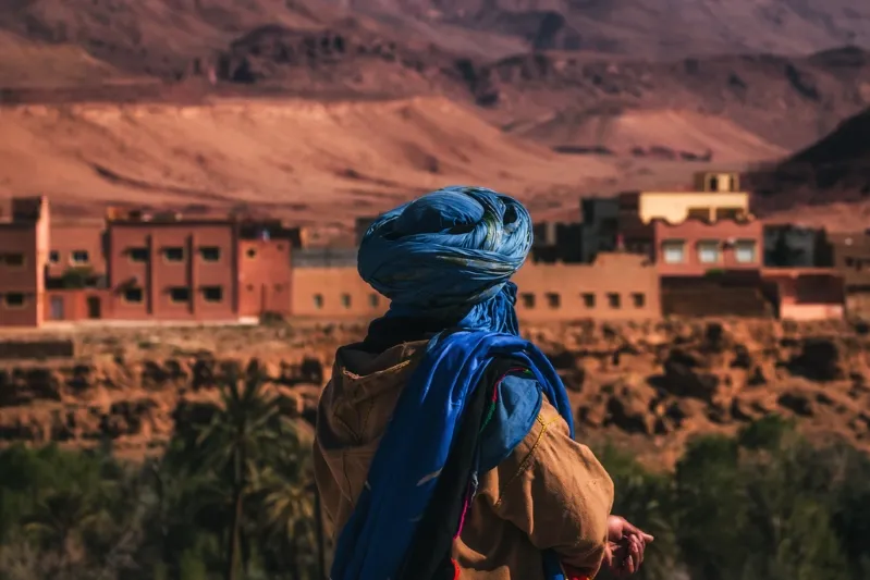 A man wearing a blue turban stands in a desert landscape, highlighting a family-friendly travel destination.