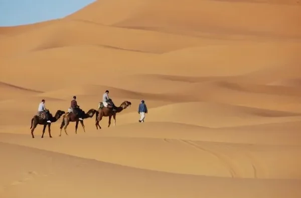 Three people ride camels through a vast desert landscape during a journey from Ouarzazate to Marrakech.
