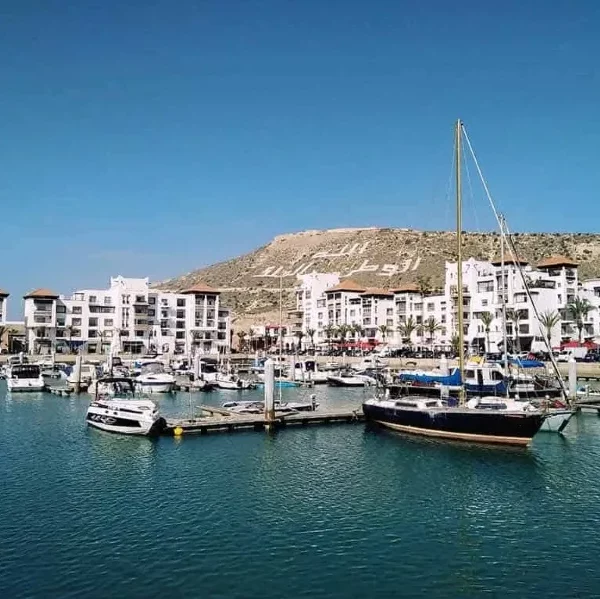 Boats are docked in a marina with nearby buildings, showcasing a scenic view of Agadir.