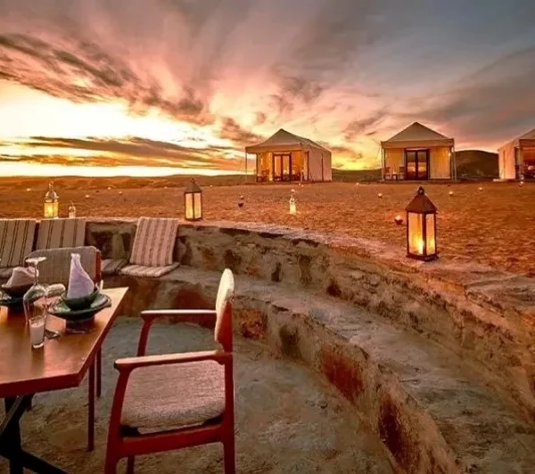 A table and chairs set on the beach at sunset, with warm hues illuminating the scene, promoting relaxation and tranquility.