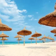 A row of thatched umbrellas on a sandy beach, inviting relaxation for Morocco Holidays 2026.