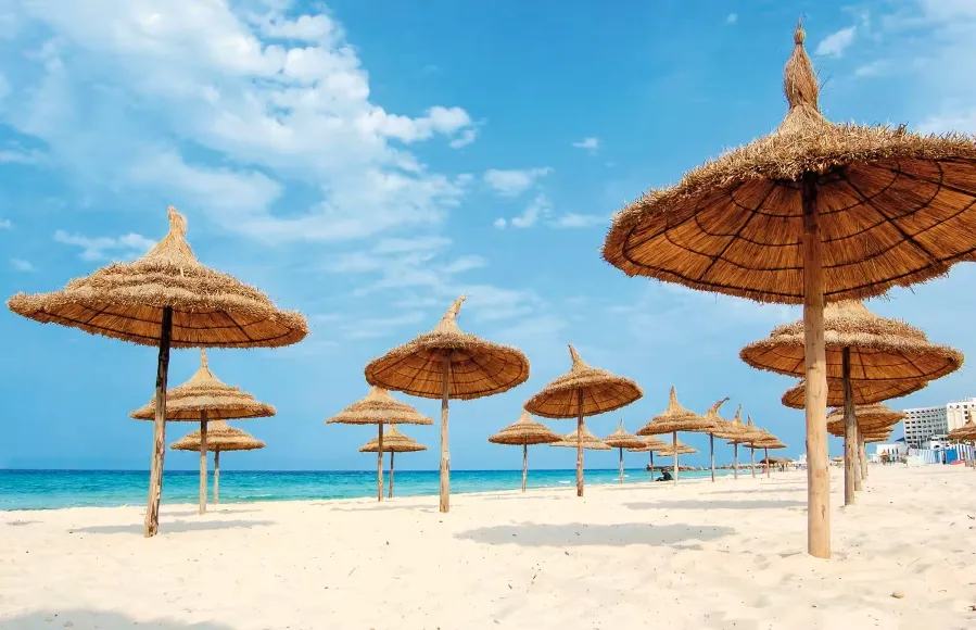 A row of thatched umbrellas on a sandy beach, inviting relaxation for Morocco Holidays 2026.