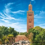Towering Koutoubia Mosque under a vivid blue sky in Marrakech, Morocco, surrounded by lush green trees, creating a serene and majestic atmosphere.