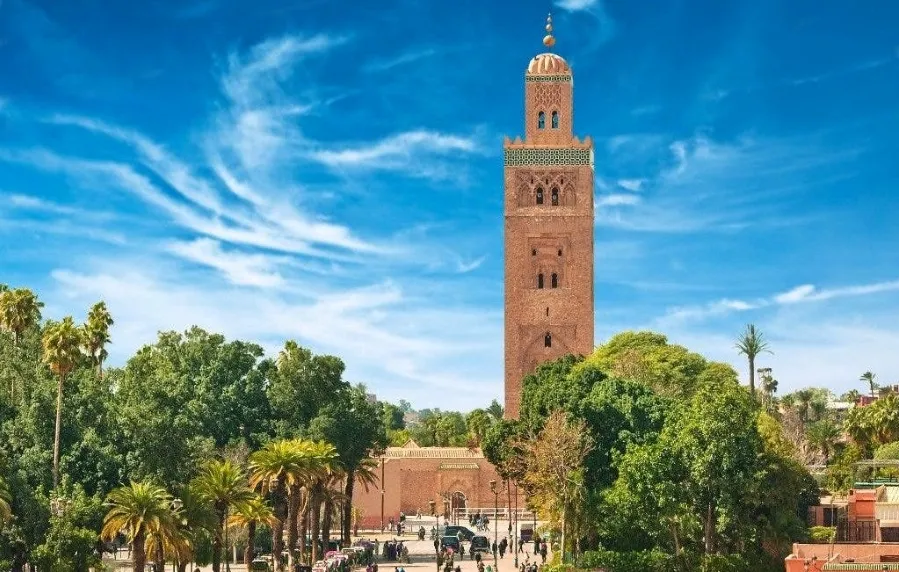 Towering Koutoubia Mosque under a vivid blue sky in Marrakech, Morocco, surrounded by lush green trees, creating a serene and majestic atmosphere.