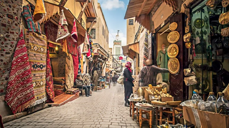 A narrow street in Marrakech, Morocco, bustling with people walking and exploring the vibrant surroundings.