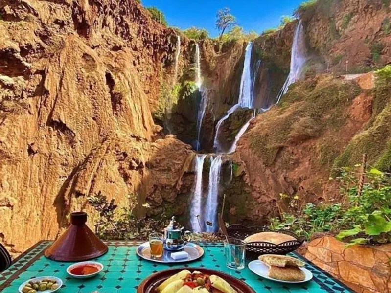 A plate of couscous served with the Ouzoud Waterfalls cascading in the background, showcasing a scenic breakfast setting.