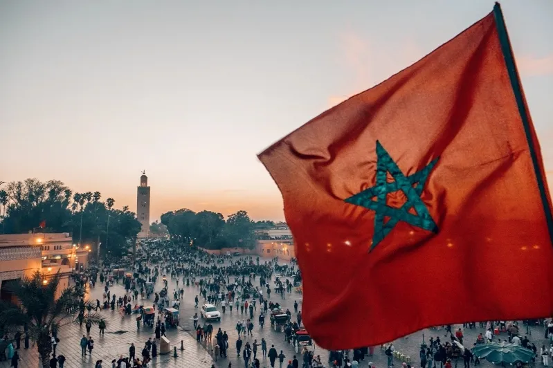 Moroccan flag waving in a cityscape of Morocco, symbolizing national pride and culture. Evisa Morocco promotion included.