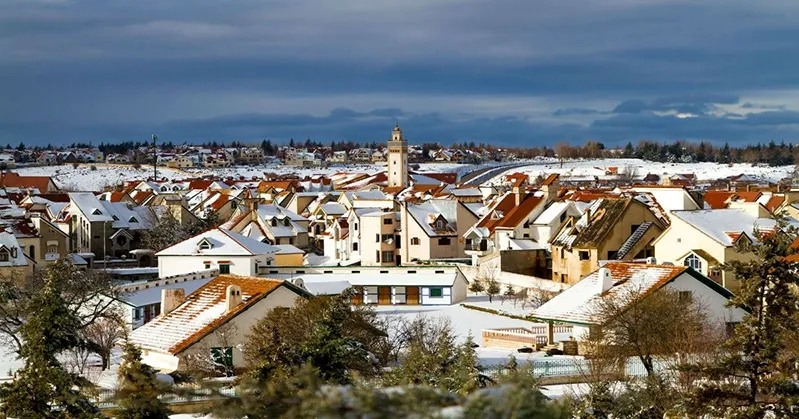 A snowy town in Ifrane, Morocco, featuring several buildings and a prominent church amidst the winter landscape.