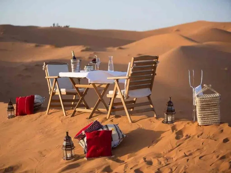 A beautifully set dinner table in the desert, surrounded by sand dunes, showcasing a unique dining experience during desert tours.