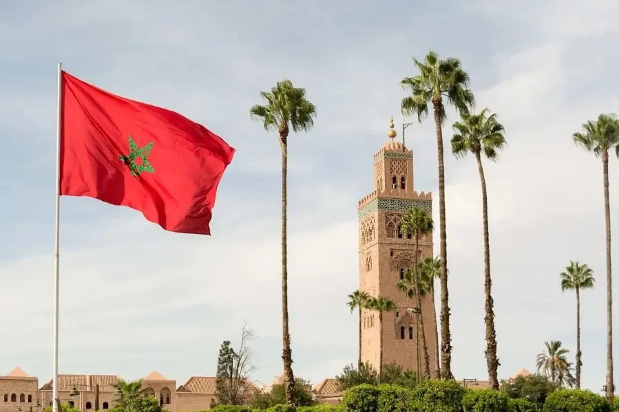 The Moroccan flag waves in front of a clock tower, symbolizing national pride and heritage.