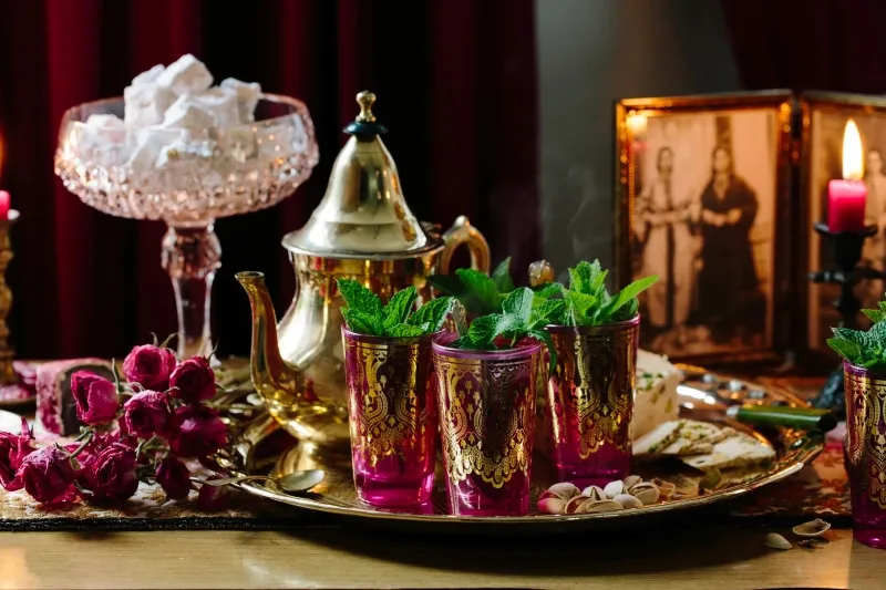 A table adorned with gold and pink decorations, candles, and a Moroccan drink, creating an elegant atmosphere.