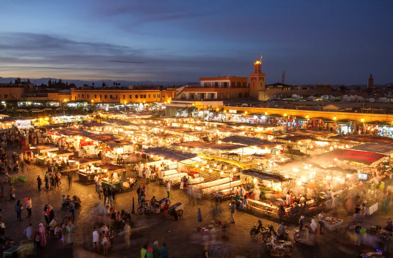 Night market in Marrakech, Morocco, bustling with vibrant stalls, colorful lights, and lively crowds enjoying local cuisine.