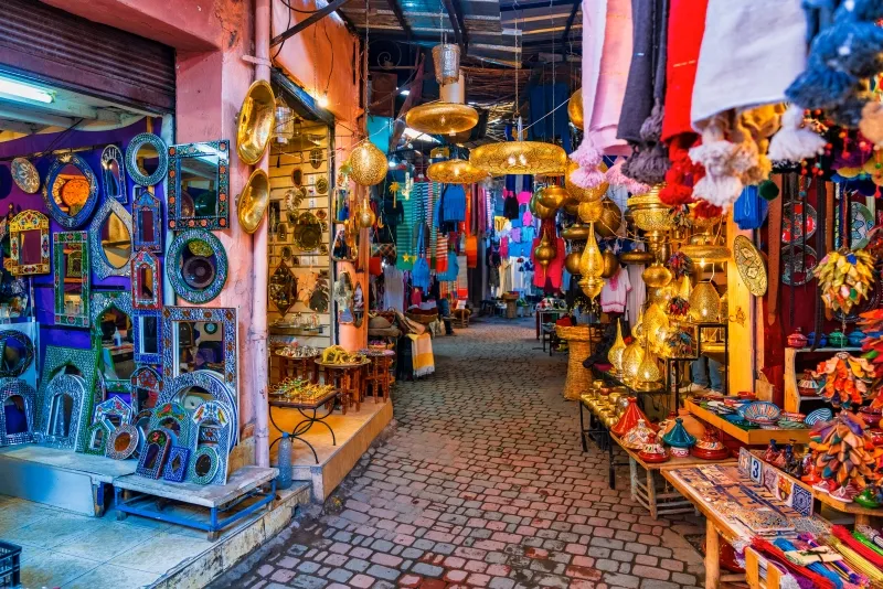 A narrow alley in Marrakech lined with vibrant, colorful items for sale, showcasing local culture and craftsmanship.
