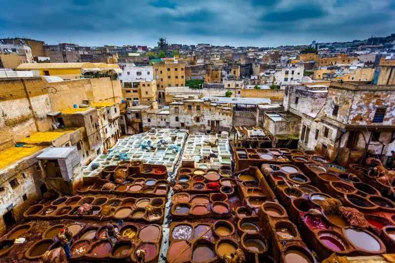 Fes A bustling Moroccan city scene featuring an array of colorful pots and pans displayed in a market setting.