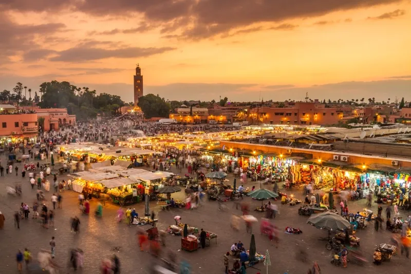 Jemaa el Fnaa Square (1) Bustling market square at sunset in Marrakesh, Morocco, with colorful vendor stalls and blurred motion of crowds, exuding a lively, warm atmosphere.Between marrakech things to see