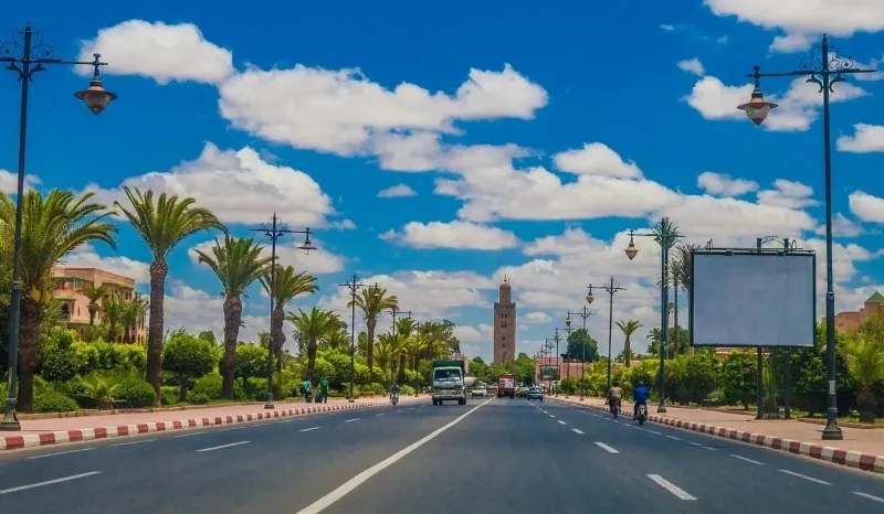 Marrakech A view of a road leading to a clock tower, set in a bustling city in Morocco.