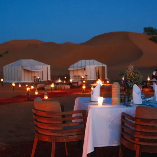 A candlelit dinner table arranged in the desert, highlighting an enchanting atmosphere for Marrakech desert tours.