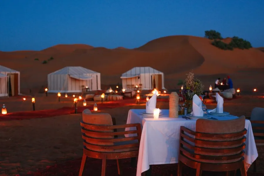 A candlelit dinner table arranged in the desert, highlighting an enchanting atmosphere for Marrakech desert tours.