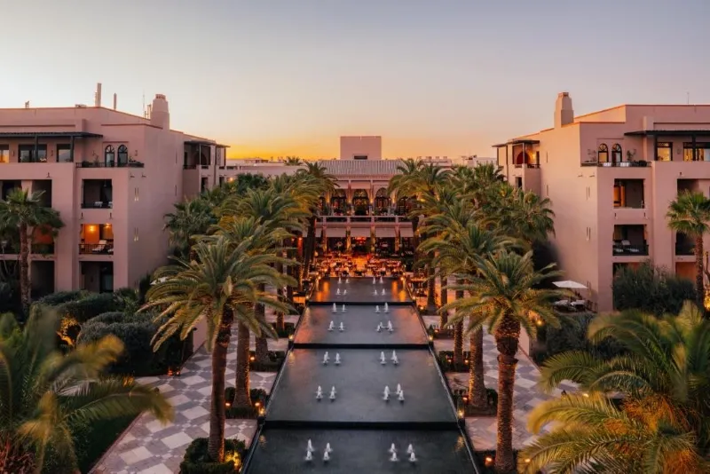 Sunset over a Moroccan resort featuring palm trees and a tranquil pool, creating a serene vacation atmosphere.