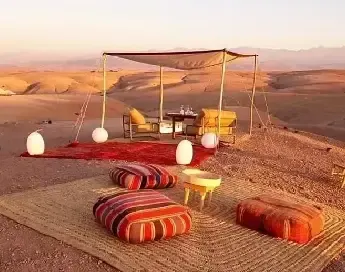 Romantic candlelit dinner table setup in the Sahara dunes with campfire and Berber music